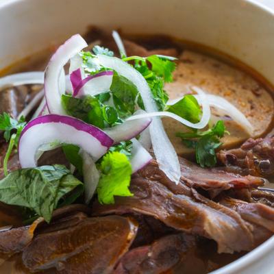 Vietnamese beef noodle soup topped with sliced red onions, cilantro and basil.