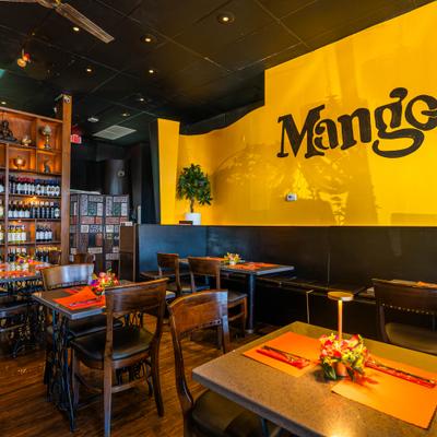Warmly lit restaurant interior with yellow walls, wooden furniture and decorative shelving..
