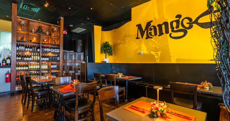 Warmly lit restaurant interior with yellow walls, wooden furniture and decorative shelving.