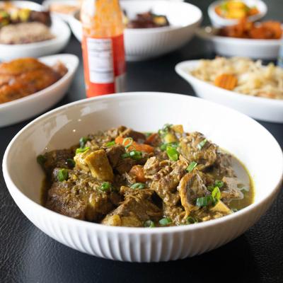 Bowl of Curried Goat served alongside other dishes.