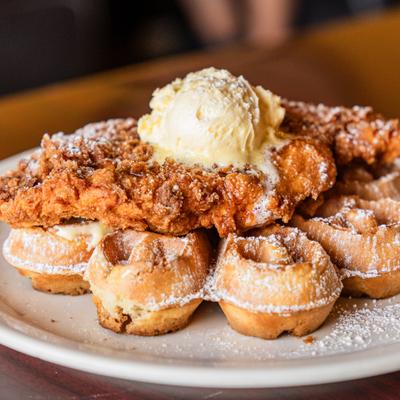 Chicken and waffles topped with a dollop of butter and powdered sugar.