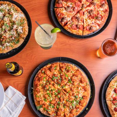 Overhead view of various pizzas served with beer and a cocktail.