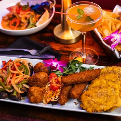 A colorful plated meal with fried plantains, fried okra, and a cocktail.