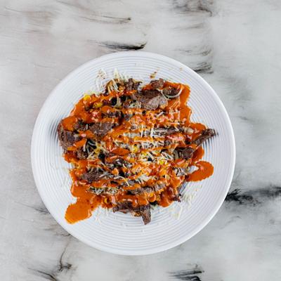 A plate of loaded steak  savory dish topped with melted cheese and a red sauce.