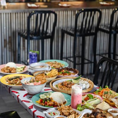 A vibrant feast of Southeast Asian dishes served on a chili-patterned table.