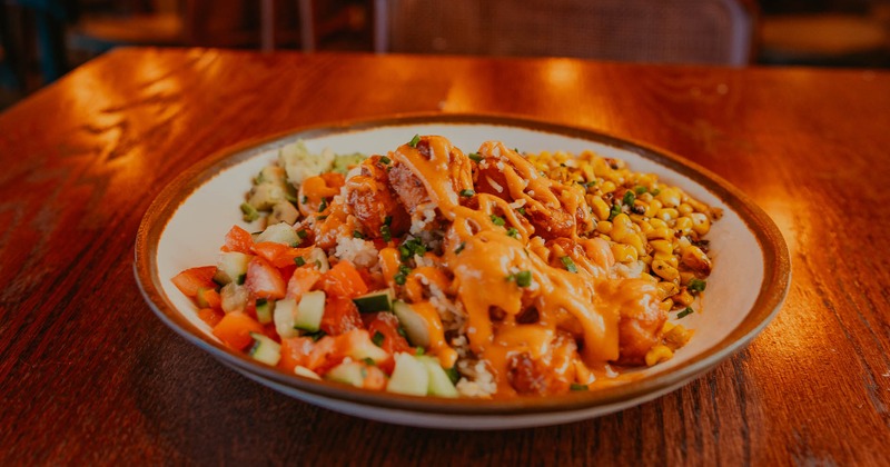 Vegan bowl with tofu, rice, cucumbers, tomatoes, roasted corn, and cashew aioli