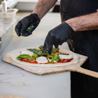 Hands in black gloves garnishing a pizza.