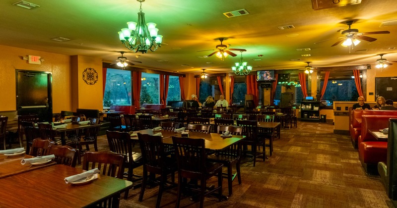 Interior of a warmly lit restaurant with wooden furniture and red curtains
