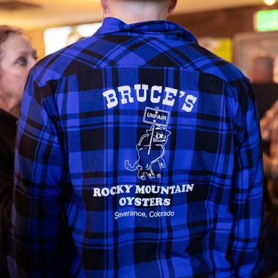 A person wearing  a blue Bruce's Bar flannel shirt.