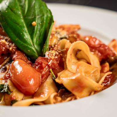 A close-up of pappardelle pasta topped with cherry tomatoes, basil, and cheese.