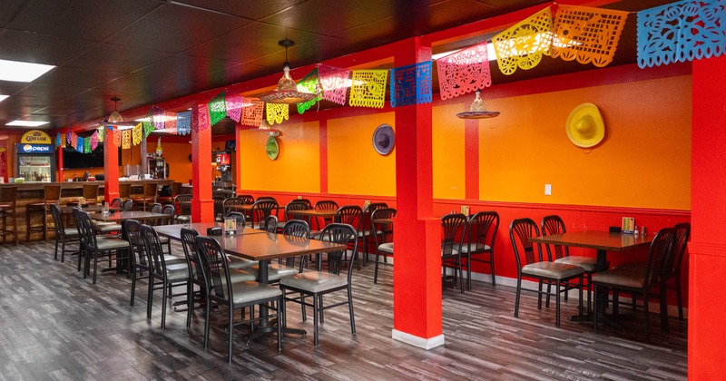 A vibrant restaurant interior with orange and red walls, black tables and chairs, and a bar area