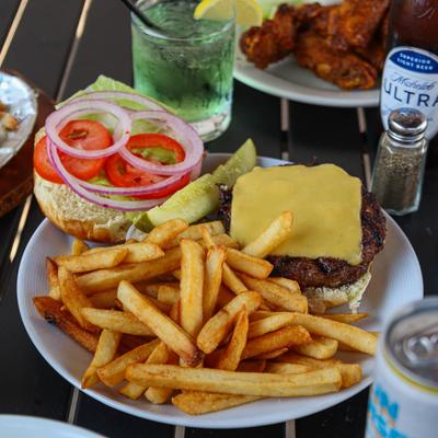 A cheeseburger with fries on a plate surrounded by various drinks and food plates.