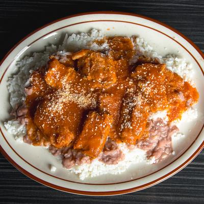 Chicken in orange sauce with rice and refried beans on a plate.