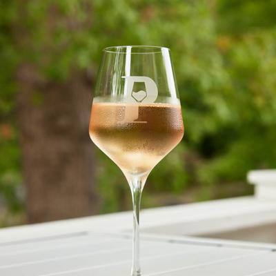 A glass of rosé wine served on a white table with greenery in the background.