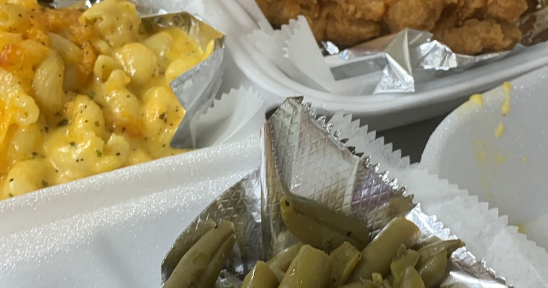 Takeout containers with mac and cheese, green beans, and fried chicken
