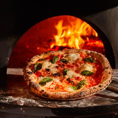 Freshly baked margherita pizza pulled out of the wood-fired oven with visible flames.