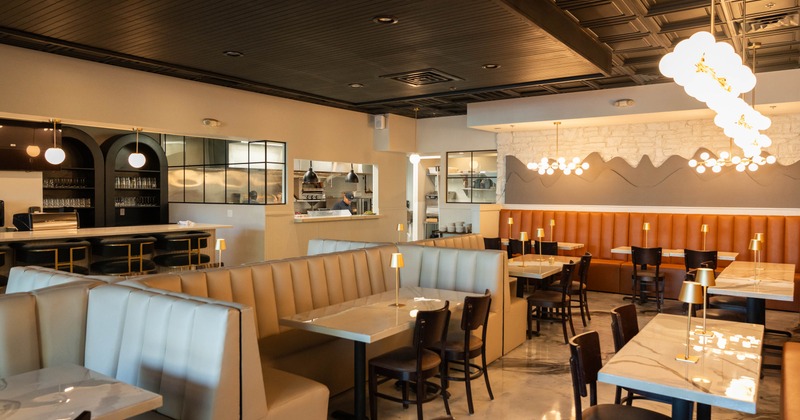 Interior of a modern, warmly lit restaurant with booth seating, marble tables