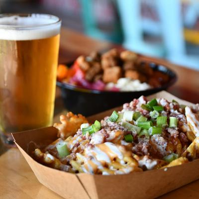 Loaded fries topped with melted cheese, bacon, and scallions, served alongside a pint of beer.