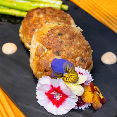 Crab cakes served with asparagus and edible flowers on a black plate.