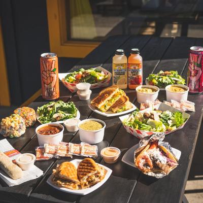 Assorted sandwiches, salads, soups, and drinks served on an outdoor table.
