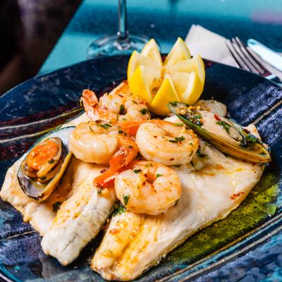 Roasted fish fillet topped with shrimp and mussels, served with carved lemon.