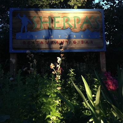 Outdoors, evening, Sherpa's logotype board sign with flowers and plants in front