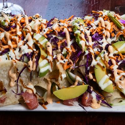 Poke nachos topped with avocado, shredded carrot, purple cabbage, and sauce drizzle.