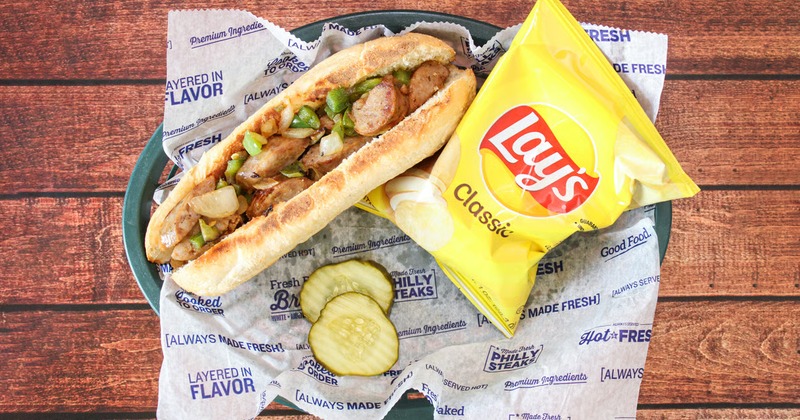 Sausage sandwich with sauteed peppers and onion, served with a bag of chips