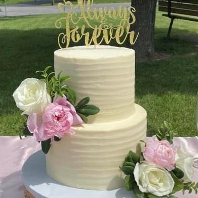 A two tiered wedding cake with floral decorations, sitting on a table in the day time