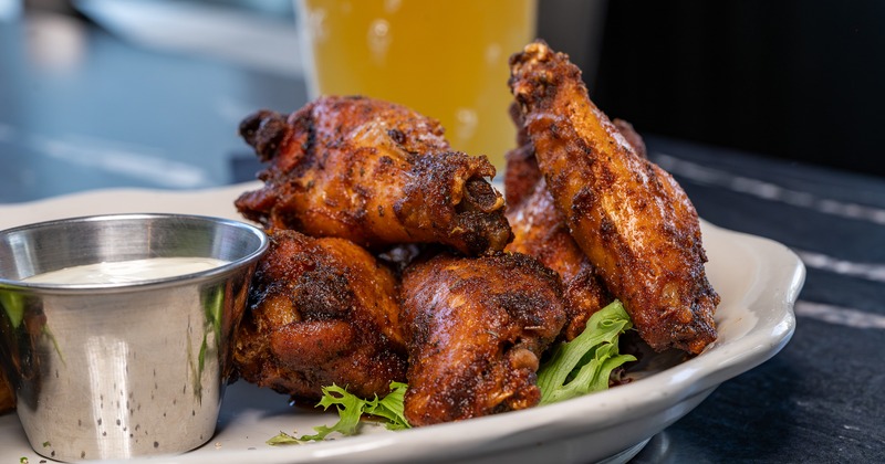 Chicken wings served with celery sticks and a dip, beside a glass of beer