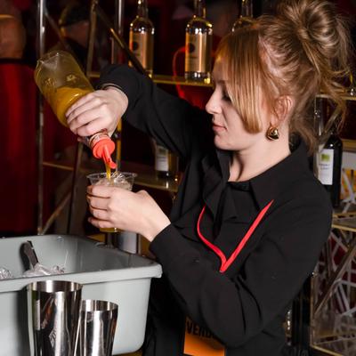 Bartender pouring orange mixer into a small cup.