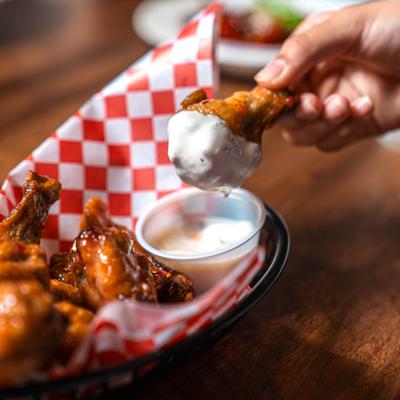 Chicken wing being dipped in a creamy white dressing.