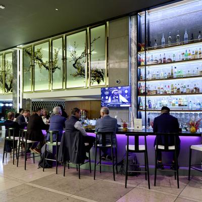 A modern bar scene with five people seated on stools, lit by purple underlighting.