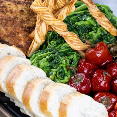 Chicken cutlet grazing board with roasted red peppers, marinated cherry peppers, and bread.