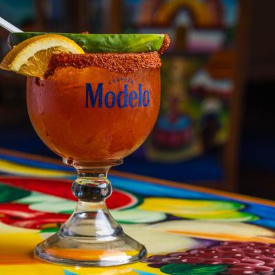 A glass of Michelada with lemon, cucumber garnish, and spiced rim.
