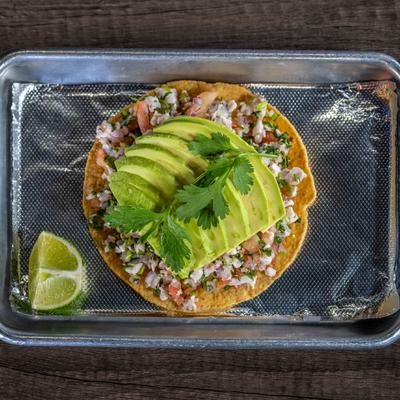 Ceviche tostada on a metal tray with lime, top view.