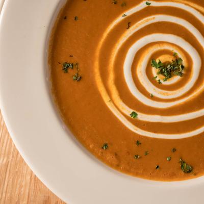 A plate of creamy, reddish-orange soup, garnished with a swirl of cream and fresh herbs.