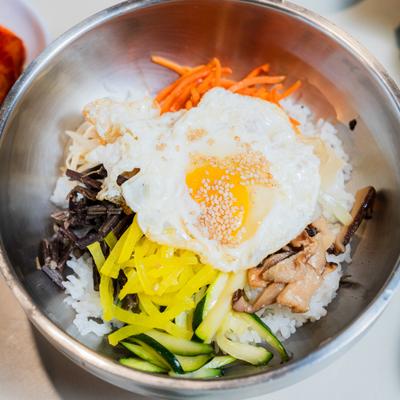 Bibimbap bowl, rice topped with various vegetables, meat, and a fried egg.