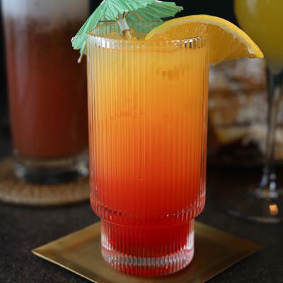 A layered orange and red cocktail, garnished with an orange slice and umbrella.