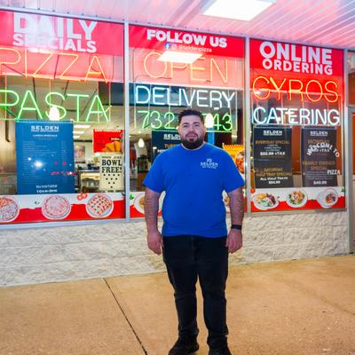 Chef standing outside the restaurant with neon signs on the windows.