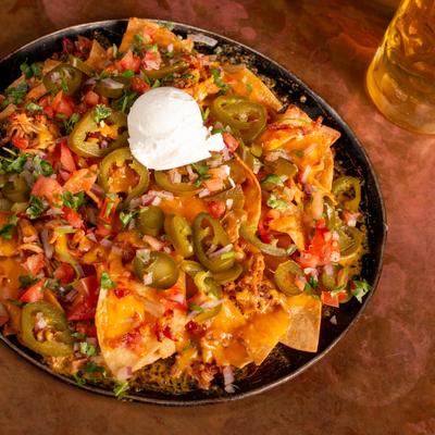 Nachos topped with cheese, jalapenos, tomatoes, and onions, served with a beer.