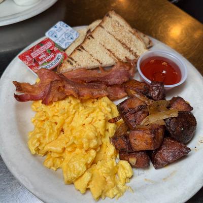 Breakfast plate with scambled eggs, bacon, potatoes, sauces and toasted bread.