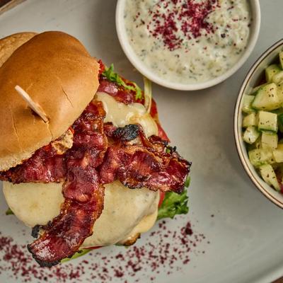 Bacon cheeseburger with cucumbers and dip on the side.