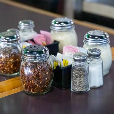 Condiment shakers with chili flakes, grated parmesan cheese, oregano and salt.