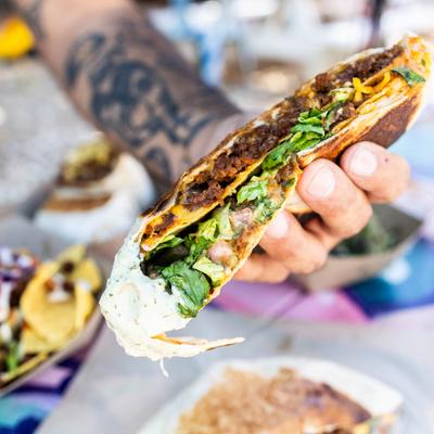 Hand holding a Crunch Wrap above the table filled with various dishes.