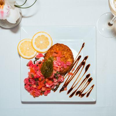 Tuna tartar with chopped tomatoes, crispy risotto cake, lemon slices, and sauce drizzle.