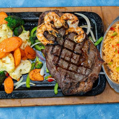 Grilled ribeye steak with grilled shrimp, seasoned rice, and vegetables.