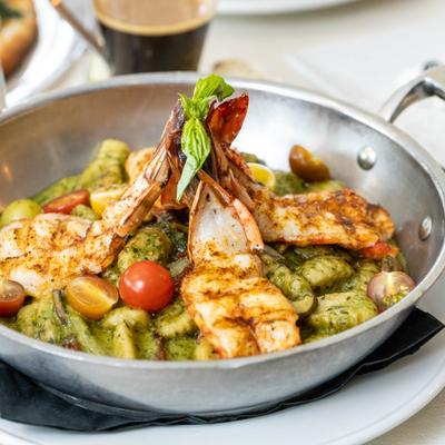 Pesto gnocchi with grilled jumbo shrimp and cherry tomatoes in a metal bowl.