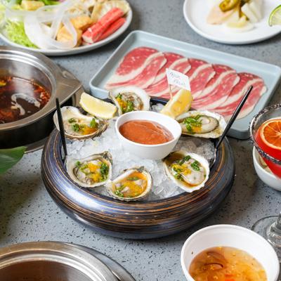 Oysters served on a bed of ice with a red sauce and lemon wedges.