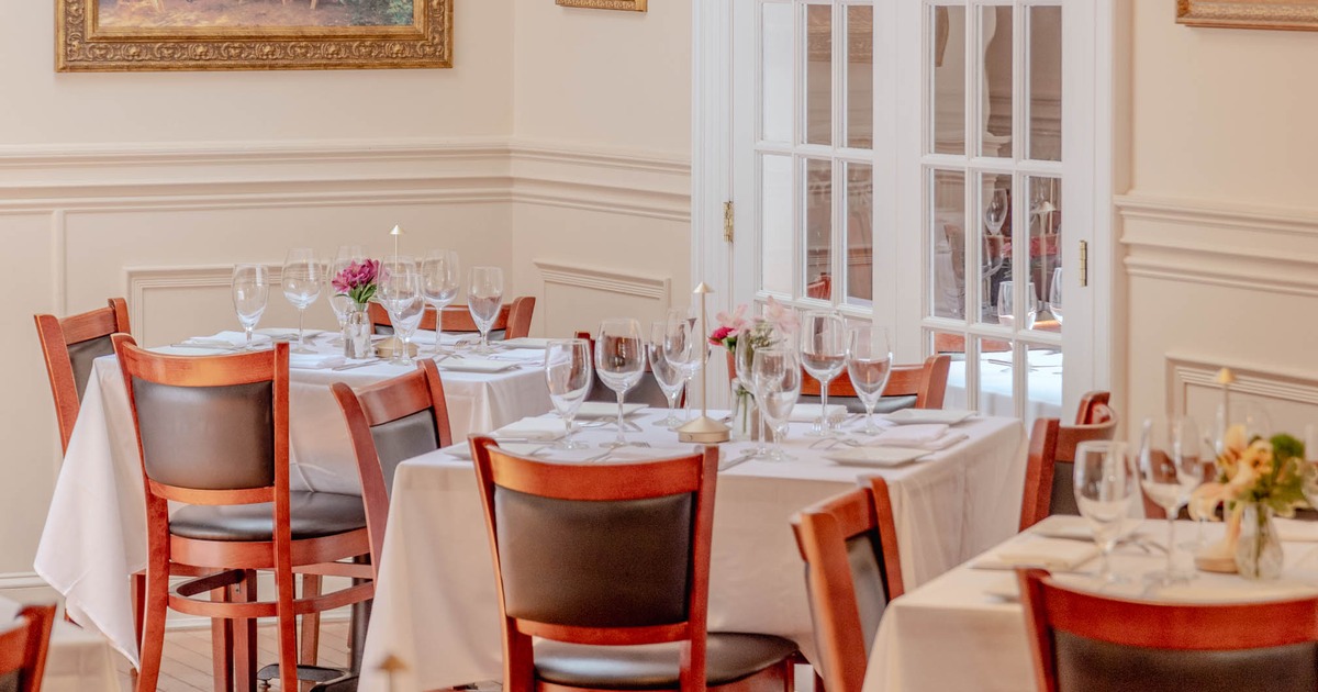 A beautifully arranged dining room with wooden tables covered in white tablecloths, glassware